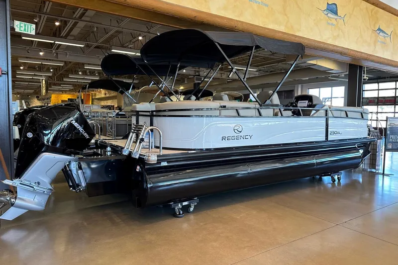 Slide: The Image of 2025 Regency 230 DL3 pontoon boat displayed indoors with Mercury outboard motor. - 2