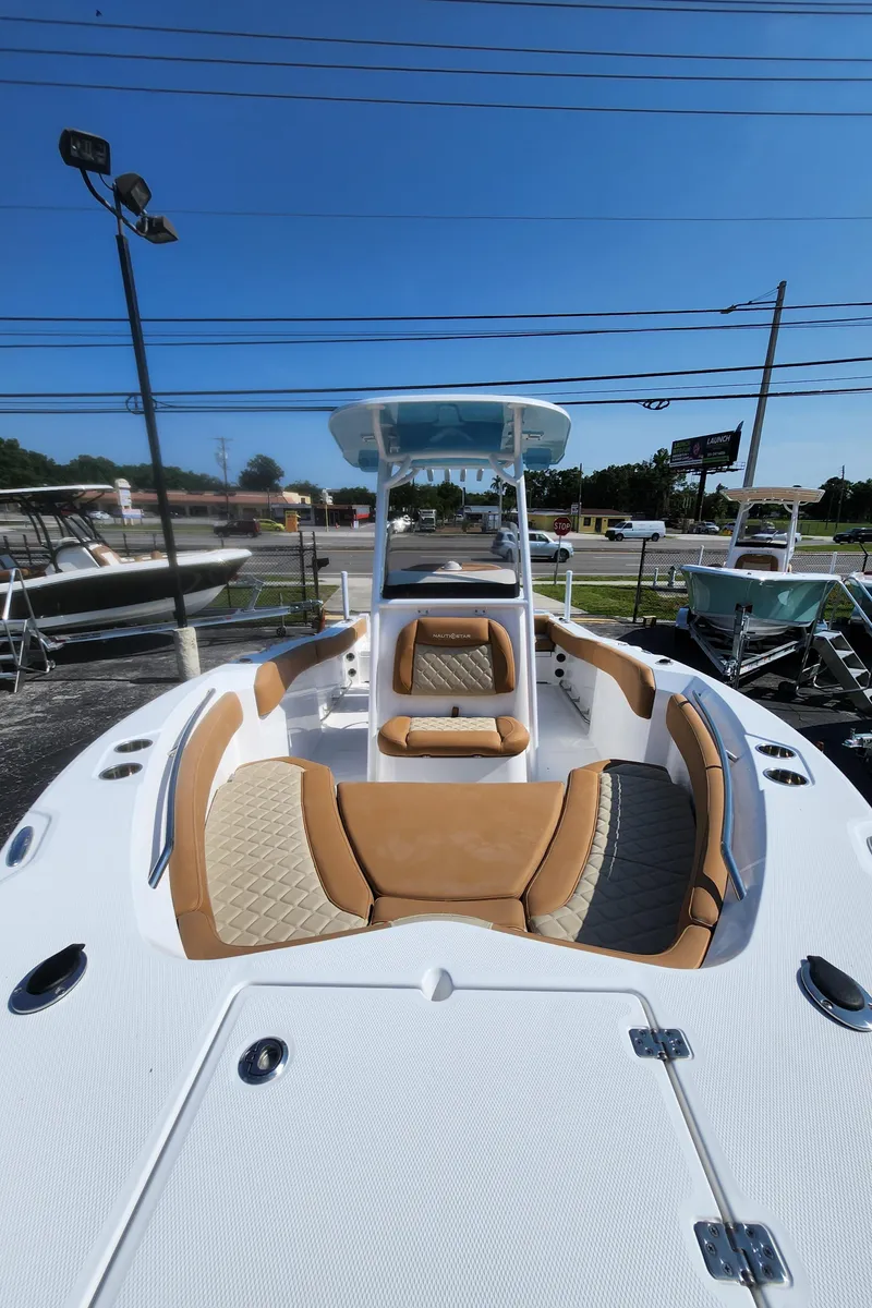 Slide: The Image of 2025 NauticStar 222 OSL boat with tan seating, showcased outdoors under clear blue sky. - 12