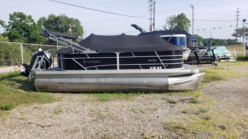 The Image of 2023 Sweetwater SW2086c pontoon boat with cover, parked on gravel lot. - 1