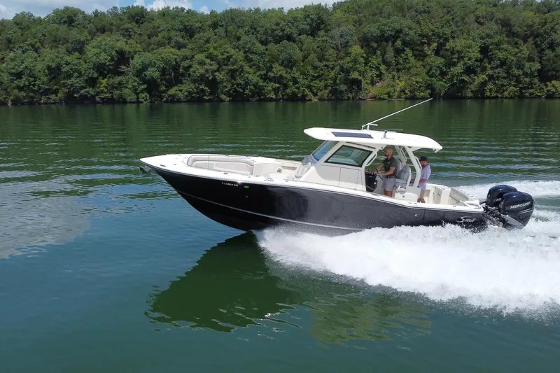 The Image of 2021 Scout 330 LXF boat cruising on a lake with lush green forest backdrop. - 0