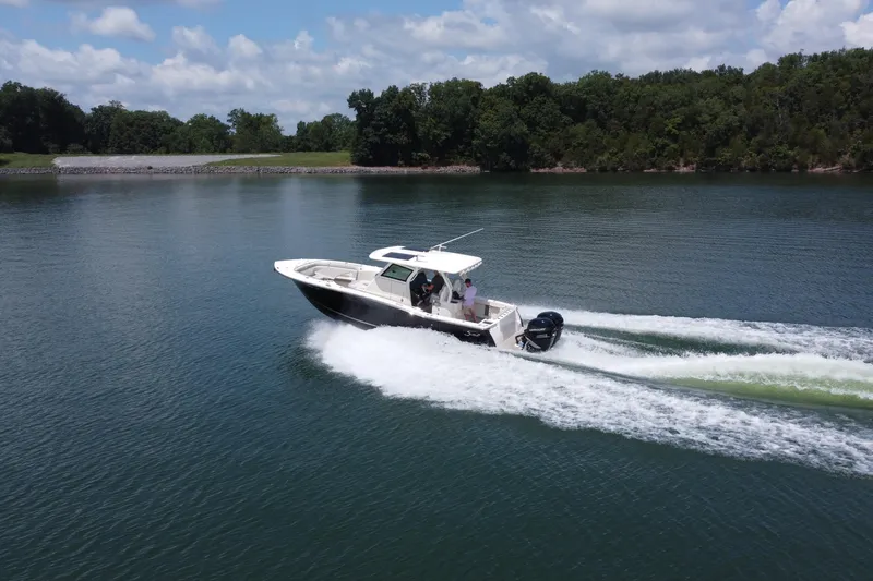 Slide: The Image of 2021 Scout 330 LXF boat cruising on a serene lake with lush green forest backdrop. - 11