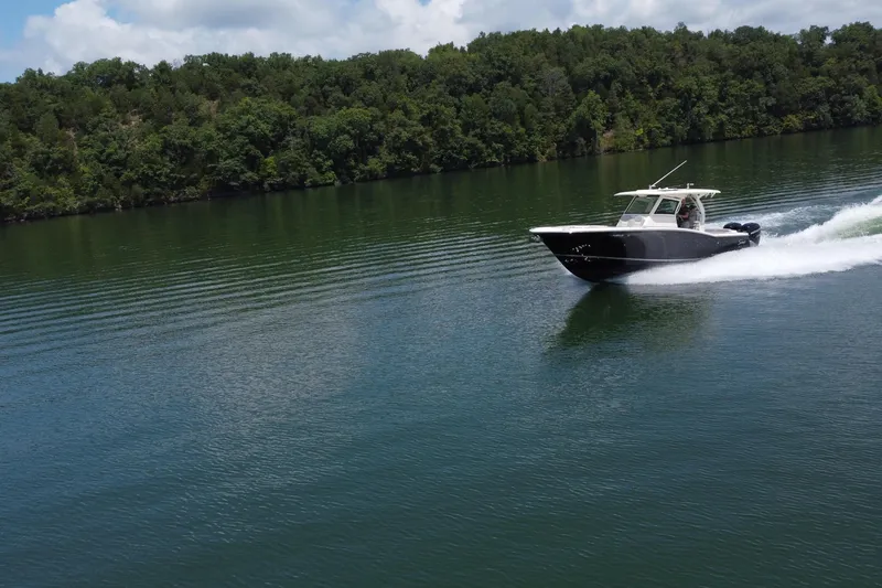 Slide: The Image of 2021 Scout 330 LXF boat cruising on a serene lake with lush green forest backdrop. - 14