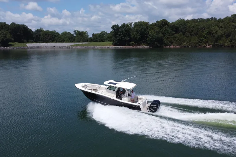 Slide: The Image of 2021 Scout 330 LXF boat cruising on a serene lake under a clear blue sky. - 15
