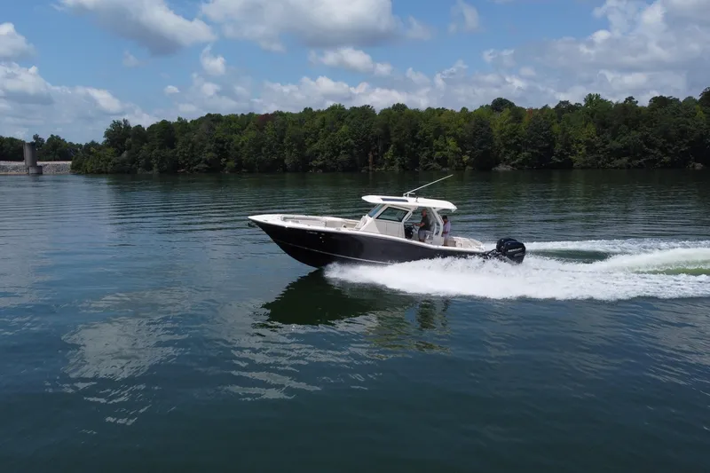 Slide: The Image of 2021 Scout 330 LXF boat cruising on a serene lake with lush green surroundings. - 8