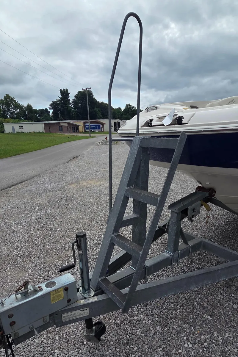 Slide: The Image of 2004 Monterey 233 Explorer boat on trailer with metal ladder, parked on gravel under cloudy sky. - 16