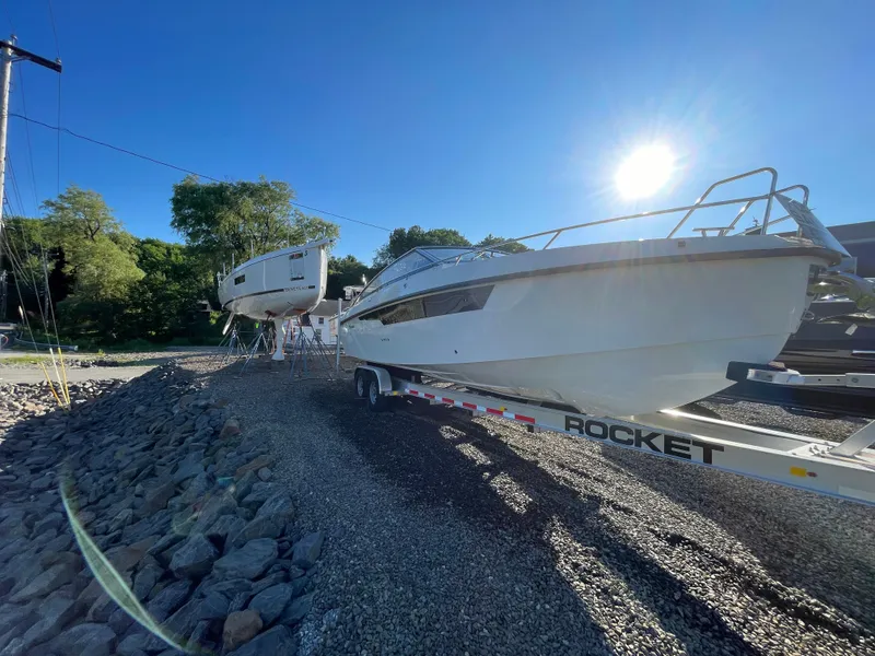 Slide: The Image of 2023 Yamarin 88 DC boat on trailer under bright sun, surrounded by trees and gravel. - 8
