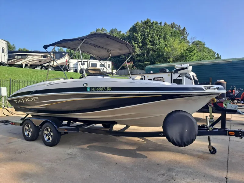 Slide: The Image of 2010 Tahoe 195 Deckboat on trailer, parked outdoors with RVs in the background. - 0