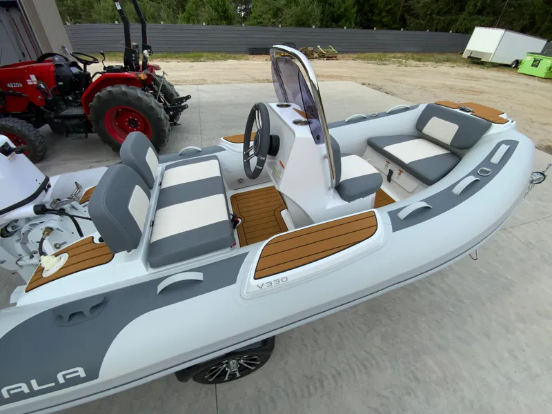 Slide: The Image of 2026 Gala V330 inflatable boat with seating, steering console, and wood accents, parked near a tractor. - 4