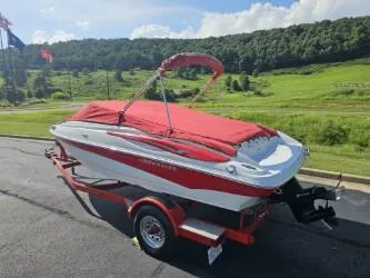 Slide: The Image of 2008 Crownline 19 SS boat with red cover on trailer, parked near lush green landscape. - 11
