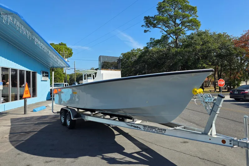 Slide: The Image of 2026 C-Hawk 25 boat on trailer outside a blue building, sunny day. - 2