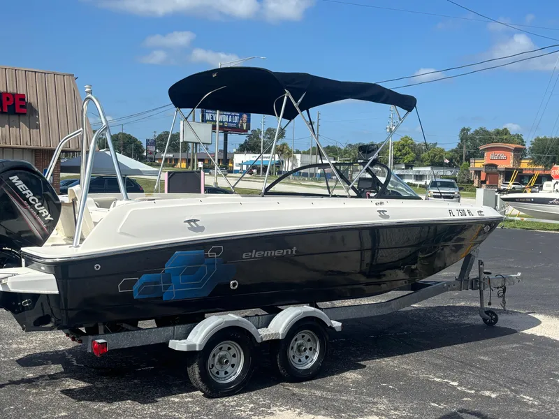 Slide: The Image of 2018 Bayliner Element F21 boat on trailer, parked outdoors under clear sky. - 16