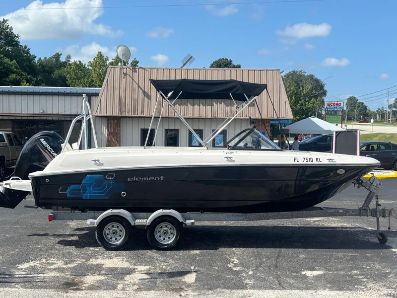 Slide: The Image of 2018 Bayliner Element F21 boat on trailer, parked outdoors, with a building in the background. - 17
