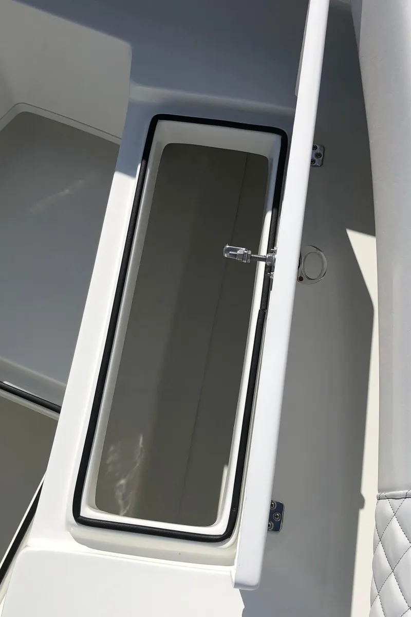 Slide: The Image of 2026 Pair Customs 24 Center Console DV boat storage compartment, open lid, white interior. - 27