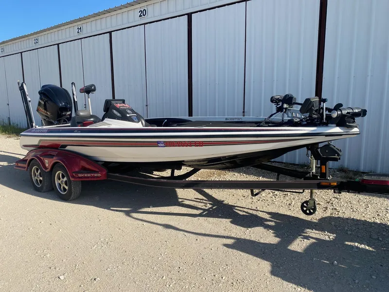 Slide: The Image of 2012 Skeeter FX 20 bass boat on trailer, parked near storage units. - 1