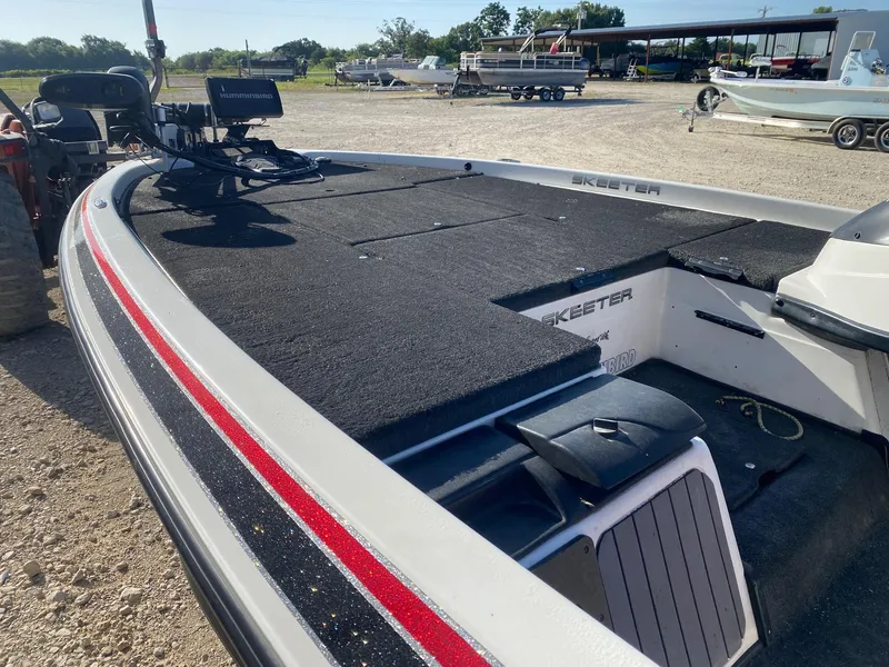 Slide: The Image of 2012 Skeeter FX 20 boat with black deck and red stripe, parked outdoors. - 7