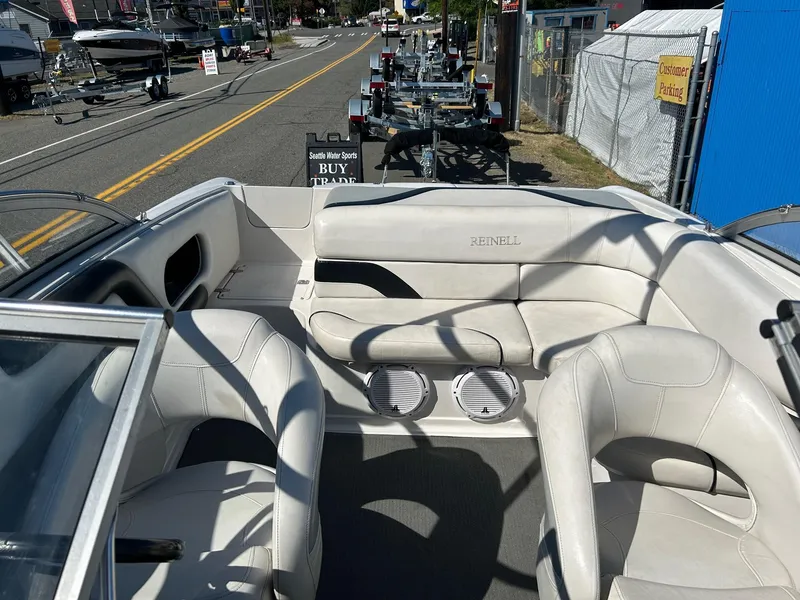 Slide: The Image of 2007 Reinell 220 LSE boat interior with white seating and speakers, parked on a street. - 9