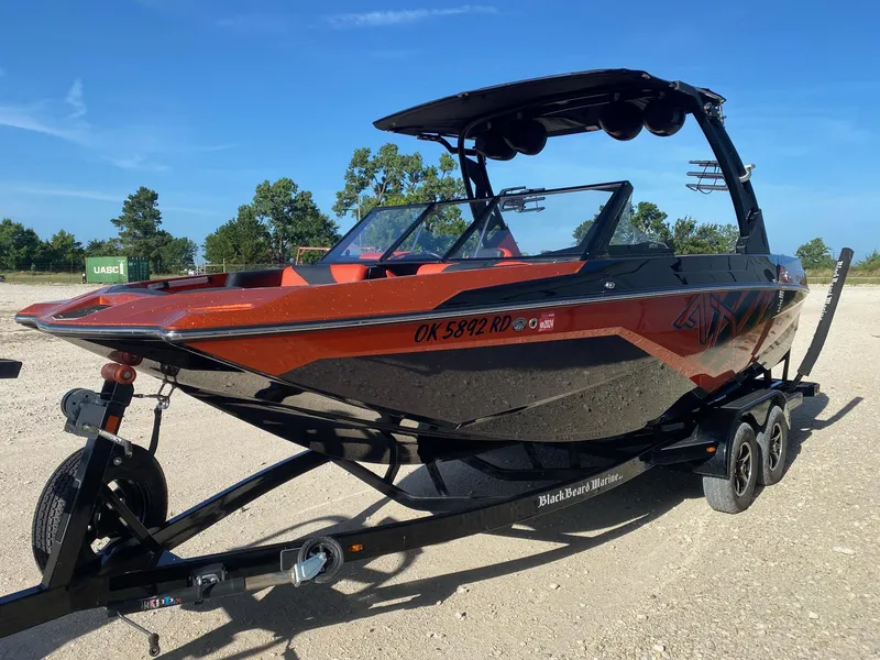 Slide: The Image of 2021 ATX Surf Boats 22 Type-S on trailer, vibrant orange and black design, parked outdoors. - 2