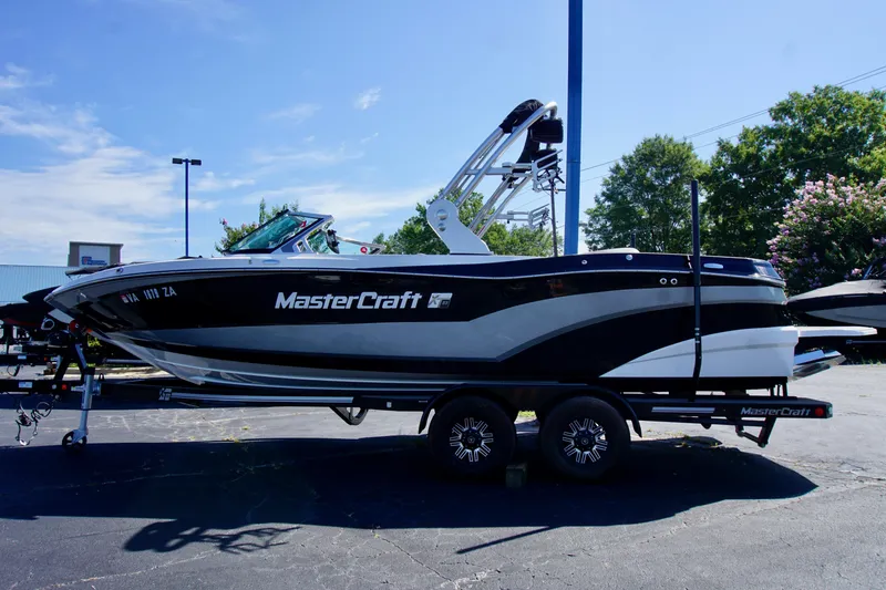 Slide: The Image of 2019 MasterCraft XT23 boat on trailer, parked outdoors under clear blue sky. - 0