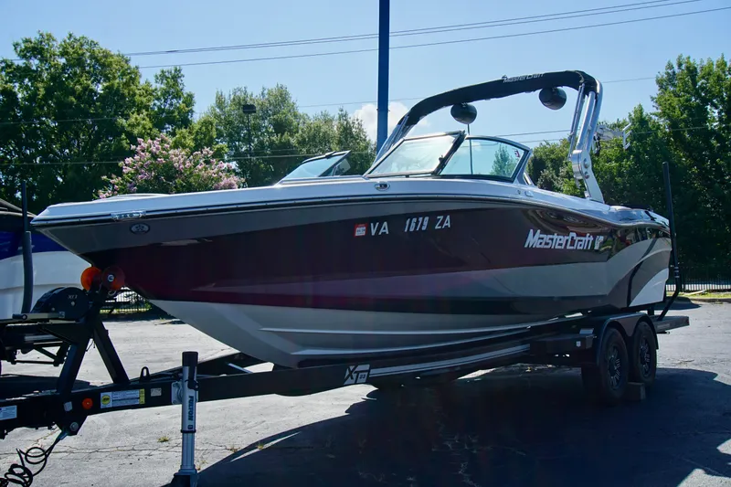 Slide: The Image of 2019 MasterCraft XT23 boat on trailer, parked outdoors with trees in background. - 3
