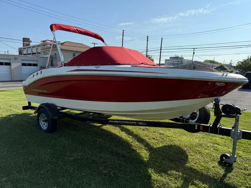 Slide: The Image of 2015 Chaparral 18 H2O Sport boat with red cover on trailer, parked on grass. - 2