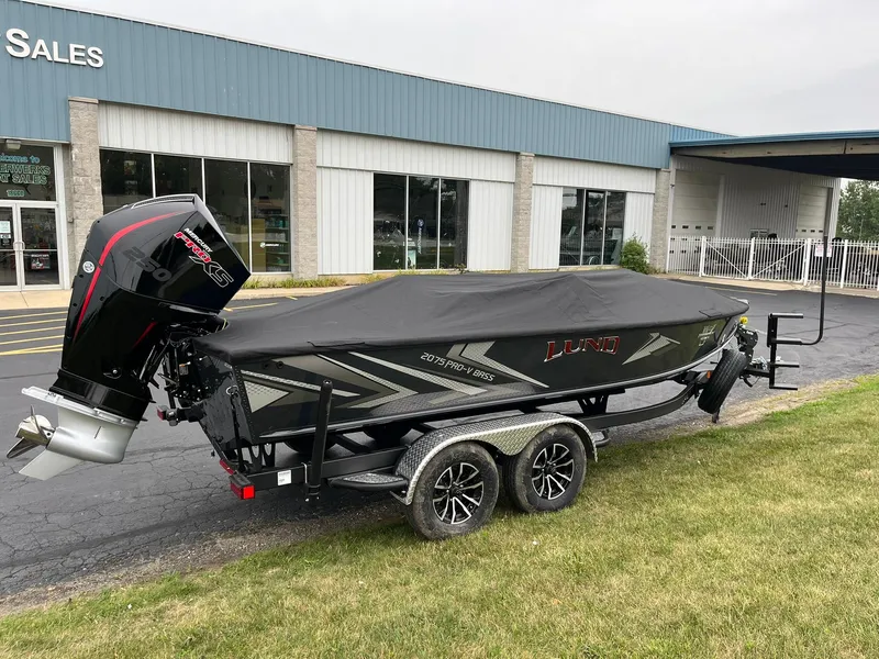 Slide: The Image of 2026 Lund 2075 Pro-V Bass XS boat with cover, parked outside a sales building. - 28
