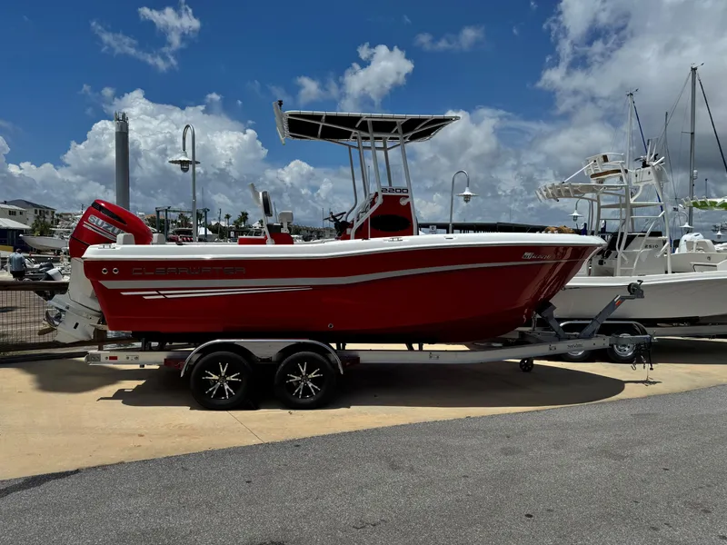 Slide: The Image of Red 2023 Clearwater 2200 boat on trailer, parked at marina under blue sky. - 2