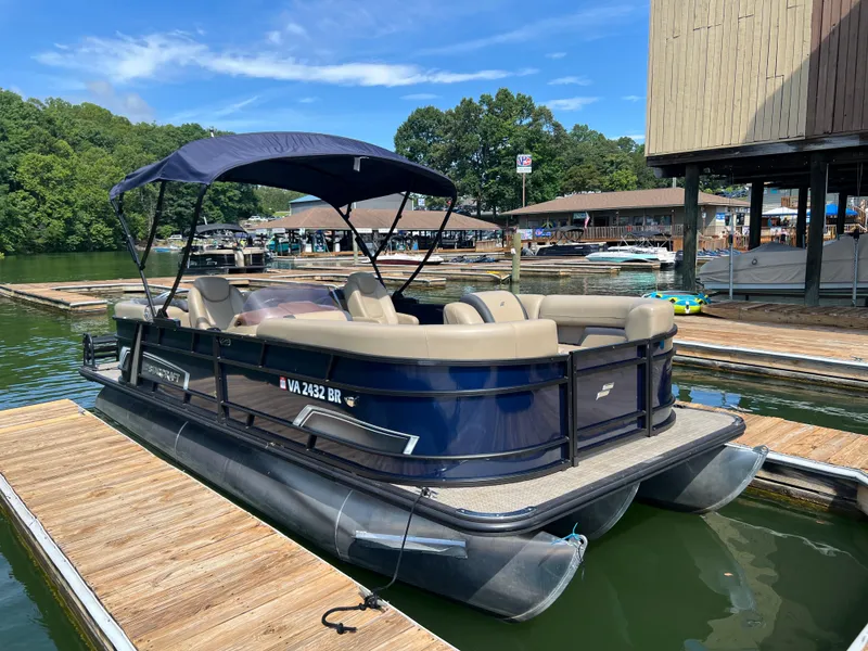 Slide: The Image of 2025 Starcraft EXS 3 pontoon boat docked at a marina on a sunny day. - 2