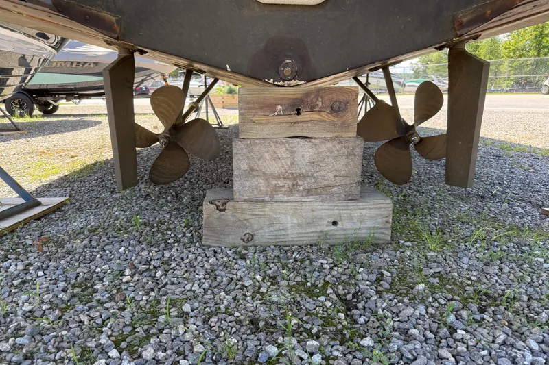 Slide: The Image of 1995 Carver 325 Aft Cabin boat propellers and rudders on gravel, supported by wooden blocks. - 20