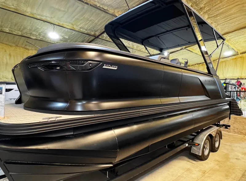 The Image of 2025 Manitou Explore pontoon boat in a showroom, featuring sleek black design. - 0