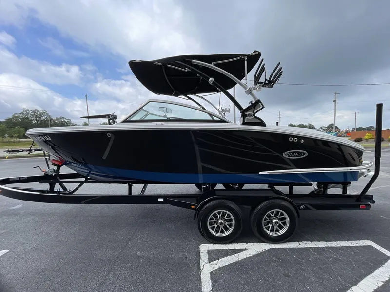 Slide: The Image of 2018 Cobalt CS23 Surf boat on trailer, parked outdoors under cloudy sky. - 2
