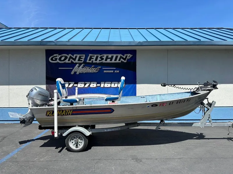 The Image of 1998 Klamath 14 DLX boat on trailer, parked outside "Gone Fishin'" store. - 1