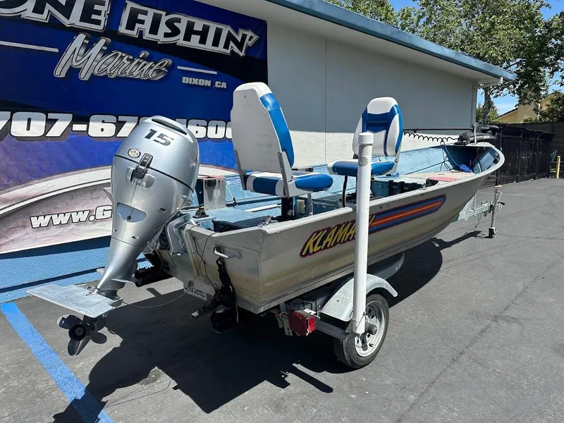 Slide: The Image of 1998 Klamath 14 DLX boat with outboard motor on trailer, parked outside marine shop. - 6