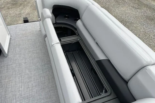Slide: The Image of 2026 Sun Tracker Party Barge 20 DLX with open storage compartment on gray seating. - 13