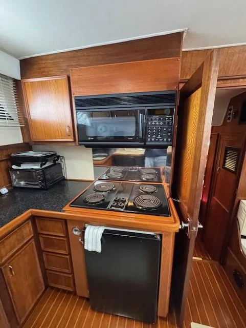 Slide: The Image of 1978 Hatteras 58 Cockpit Motor Yacht kitchen with stove, microwave, and wooden cabinetry. - 38