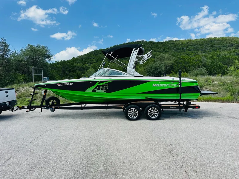 Slide: The Image of 2012 MasterCraft X-45 boat in green and black on a trailer, parked outdoors. - 6