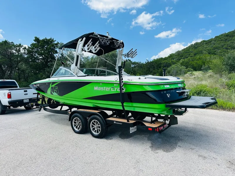 Slide: The Image of 2012 MasterCraft X-45 boat in green and black on a trailer, parked outdoors. - 8