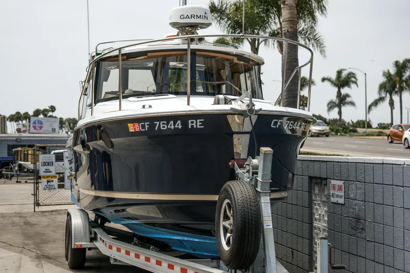Slide: The Image of 2018 Ranger Tugs R-23 boat on trailer, parked near palm trees and road. - 2