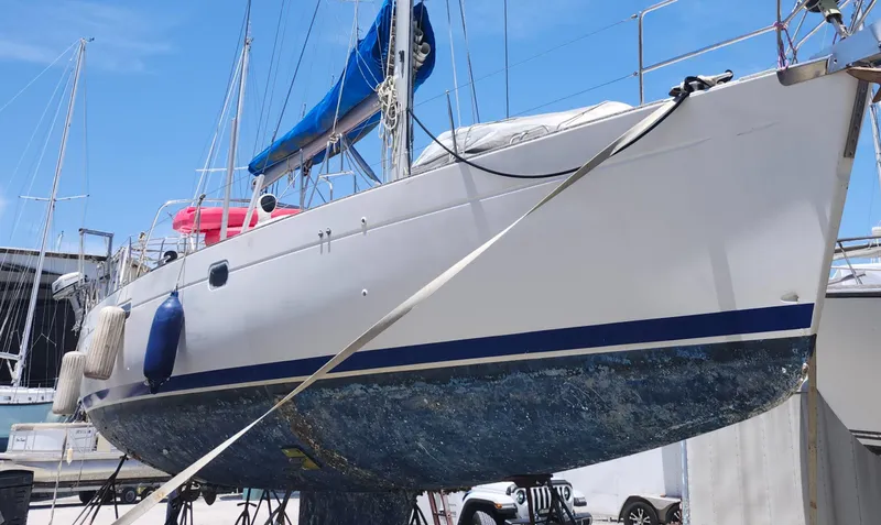 Slide: The Image of 2003 Beneteau 50 sailboat on dry dock, blue hull, white deck, clear sky background. - 3