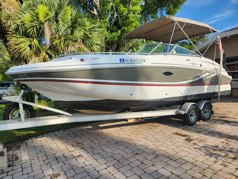 Slide: The Image of 2013 Hurricane SD2400 OB boat on trailer, parked on a paved driveway with lush greenery. - 2