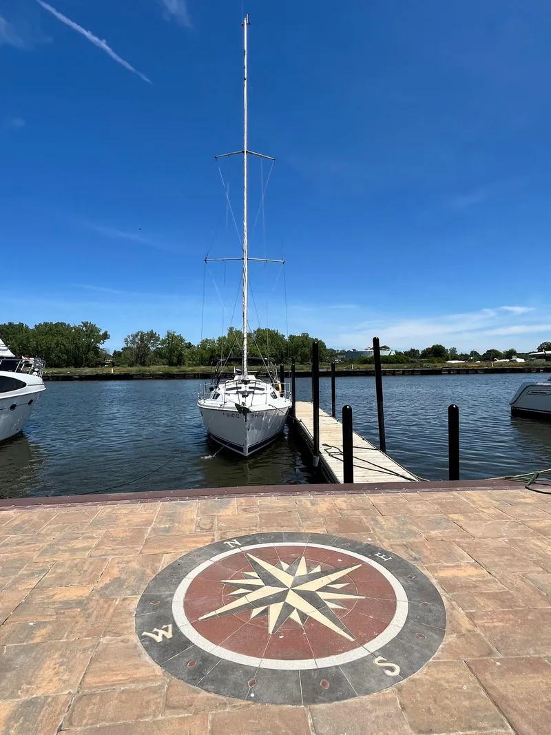 Slide: The Image of Sailboat docked by pier under clear blue sky, compass rose on pavement. Hunter 320, 2001. - 8