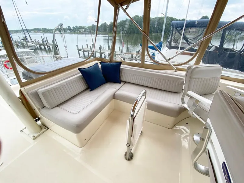 Slide: The Image of 2004 Mainship 340 boat interior with white seating and blue cushions, docked by a serene lake. - 17