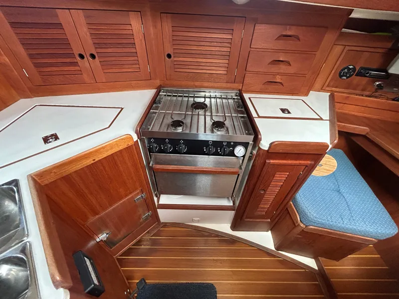 Slide: The Image of 1998 Tartan 3500 yacht interior kitchen with stove, wooden cabinets, and blue cushioned seating. - 11