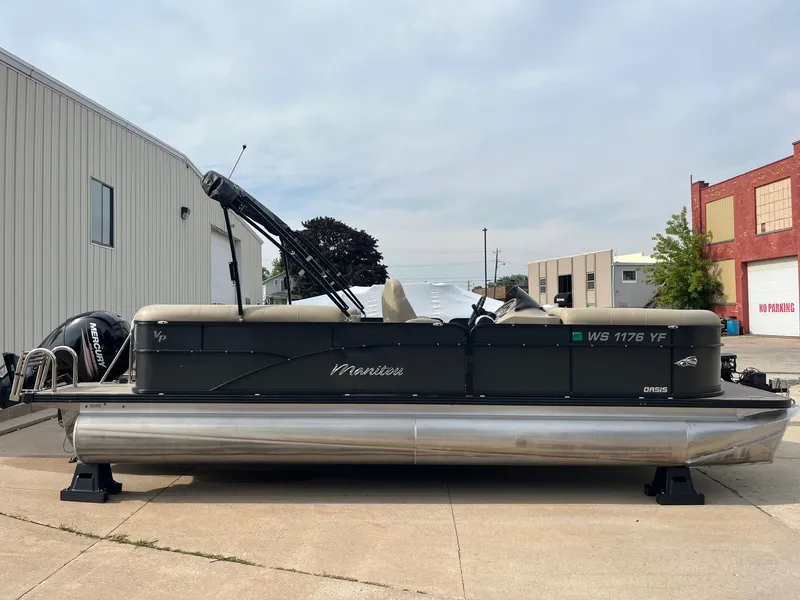 Slide: The Image of 2018 Manitou 23 Oasis RF VP pontoon boat parked outside industrial buildings. - 1