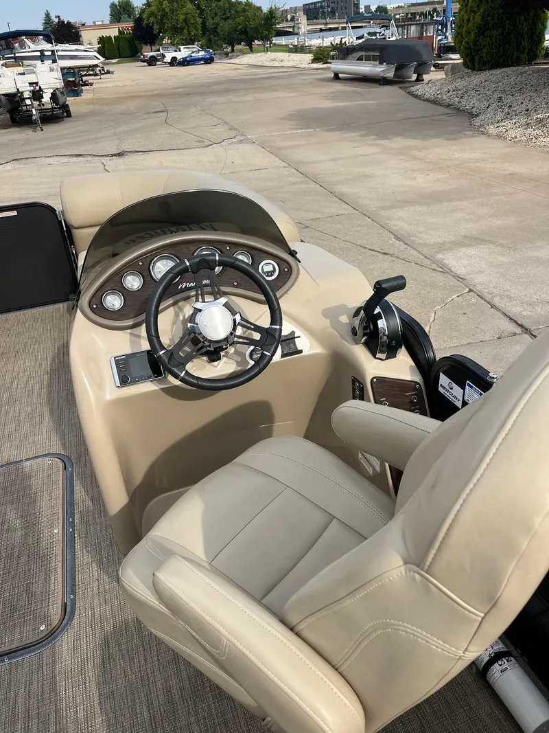 Slide: The Image of 2018 Manitou 23 Oasis RF VP boat cockpit with steering wheel and beige captain's chair. - 2