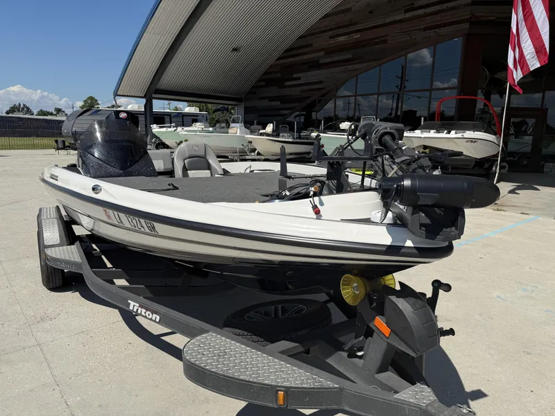 Slide: The Image of 2023 Triton 19 TrX Patriot boat on trailer, parked outdoors near a showroom. - 18