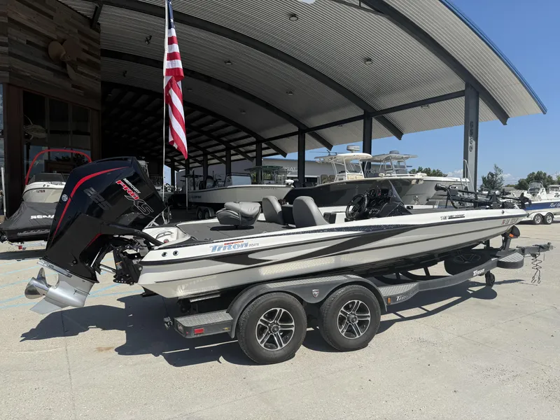 Slide: The Image of 2023 Triton 19 TrX Patriot boat on trailer, displayed outdoors with American flag. - 21