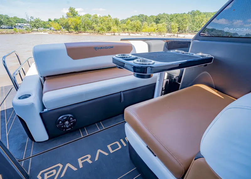 Slide: The Image of 2025 Paradigm 236 boat interior with brown and white seating, cup holders, and scenic river view. - 12