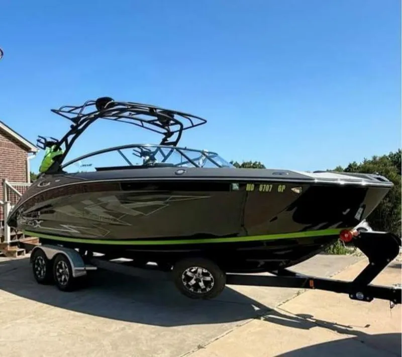 Slide: The Image of 2021 Yamaha Boats 255XD on trailer, sleek black design with green accents, parked outdoors. - 0