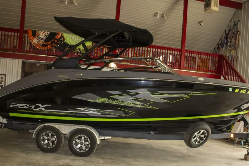 Slide: The Image of 2021 Yamaha Boats 255XD on water, rear view, with American flag and lush forest backdrop. - 24