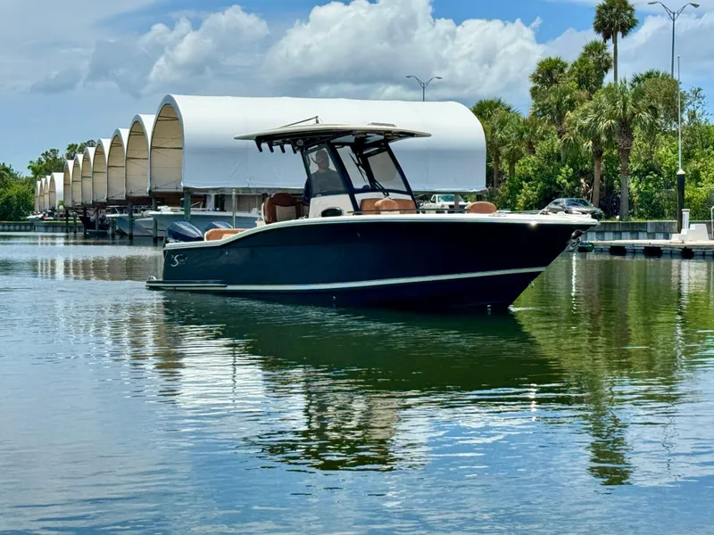 Slide: The Image of 2024 Scout 277 LXF boat on calm water near covered docks and palm trees. - 6